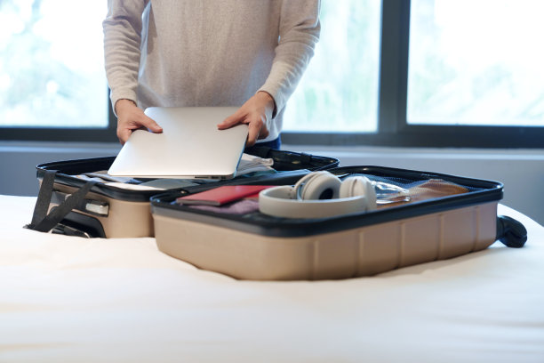 一张裁剪过的照片显示，一个女人的旅行箱里装着衣服、太阳镜、耳机、笔记本电脑和护照，放在床上图片下载