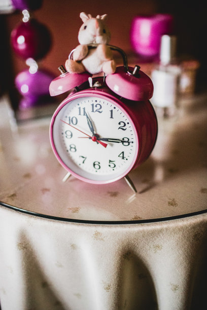 床头柜上儿童粉红色闹钟的垂直照片。图片下载