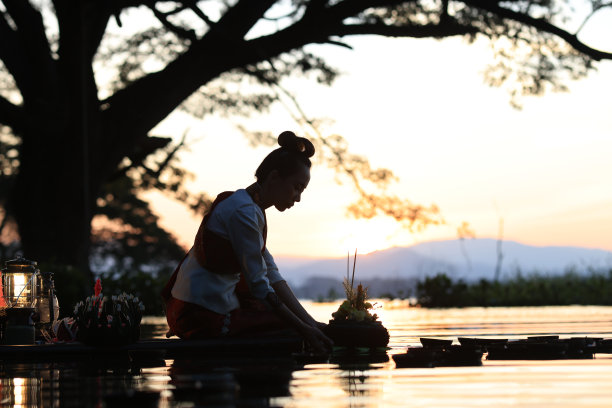 在十一月的月圆之日，一位美丽的亚洲女子在河边漂浮着一个被泰国语称为“kratong”的叶筐，向水神祈祷图片下载