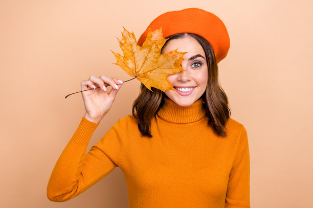可爱的可爱的满意的女士的照片走在街上享受十月十一月的天气拿干黄叶孤立在米色的背景图片下载