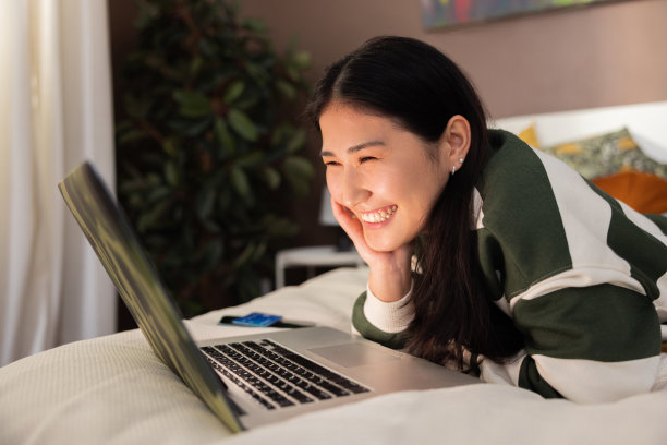 放松快乐的亚洲哈萨克斯坦女孩女士穿着休闲的衣服，微笑着看着上一部系列电影，在拍摄过程中躺在家里舒适的床上大笑图片下载