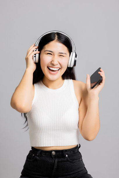 快乐的年轻少年亚洲日本妇女戴着现代的新耳机看着相机微笑放松拿在手机上听音乐图片下载