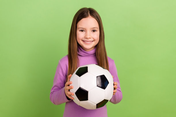 照片积极乐观的孩子长发型，穿紫色高领毛衣，手拿足球孤立的绿色背景图片下载
