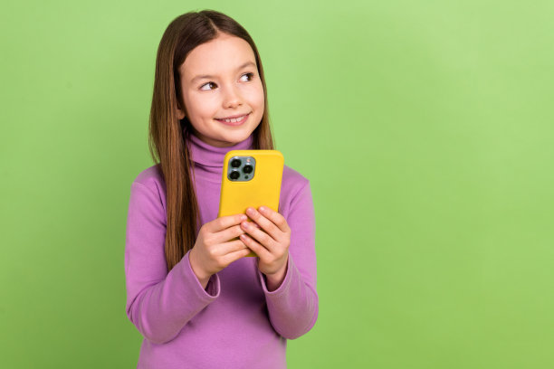 可爱的直发孩子的照片，穿着紫色的高领毛衣，看着宣传空白的空间，把智能手机孤立在绿色的背景上图片下载