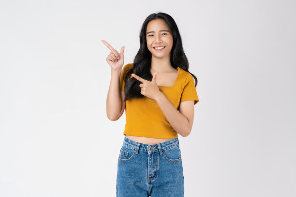 快乐微笑的年轻女子穿着休闲的橙色t恤，一只手指着上面，孤立在白色的背景上。图片下载