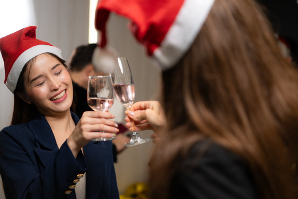 戴着圣诞帽的亚洲女人在派对上碰杯香槟图片下载