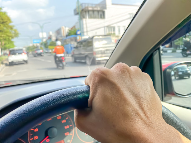 近距离的照片，男子驾驶与一个右手控制方向盘。印尼司机的第一人称视角在仪表盘内的车与拥挤的道路外面。白天的日光。图片下载
