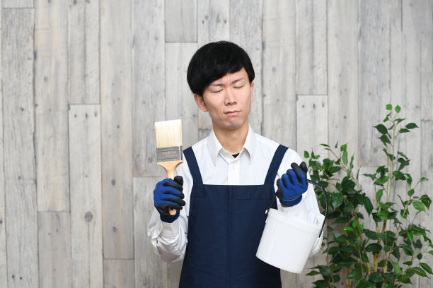 一个愁眉苦脸的亚洲年轻人，系着围裙，拿着画笔和水桶在室内图片下载