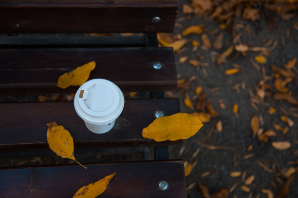 咖啡站在被秋叶包围的长凳上。秋天的温暖和舒适。暖秋照片图片下载