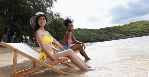 享受黑人和白人妇女坐在白色的日光浴椅上放松的热带海滩图片下载