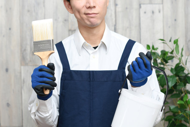 一个愁眉苦脸的亚洲年轻人，系着围裙，拿着画笔和水桶在室内图片下载