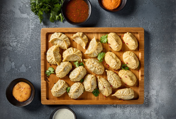 这是一张俯视图的水平照片，强调了各种各样的酱汁，以及各种各样的螳螂饺子和东方饺子，呈现在一块质朴的木板上，背景是灰色的图片下载