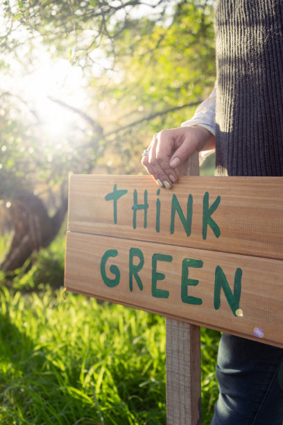 戴着帽子的年轻女子站在树木和阳光的环境中，举着一个写着“绿色思考，保护自然环境，爱护环境”的木牌图片下载