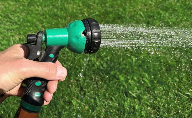 手持带喷雾器的花园软管，将水喷洒在绿草、草坪上图片下载