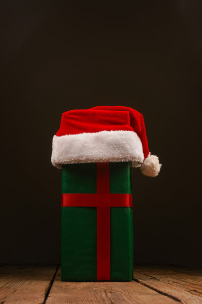 木制背景上的圣诞礼盒和圣诞老人帽的俯视图照片。圣诞背景与文字的地方。Copyspace。图片下载