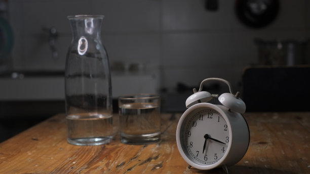闹钟的概念照片，一个杯子和一瓶水在黑暗的背景，图片下载