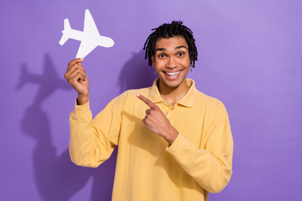 照片中开朗快乐的男子穿着时髦的黄色衣服，手示范飞机航空公司购票孤立在紫色的背景图片下载