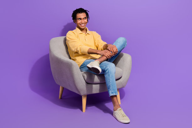 坐在椅子上的年轻人的全身照片放松，梦幻般的看着空的空间思考迷幻的想法孤立在紫色的背景图片下载