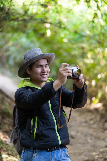 徒步旅行，亚洲旅行者拍摄美丽的照片生活方式和放松的概念年轻的亚洲男子带着灰色的背包拍摄美丽的模糊的自然照片。绿色森林地区图片下载