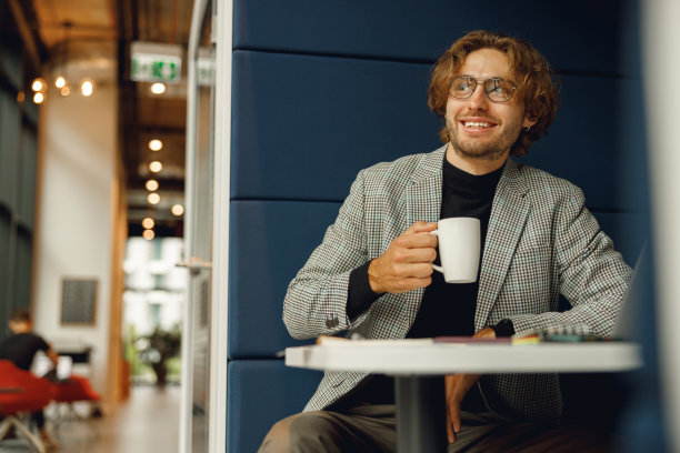 休息时间坐在办公室喝咖啡的微笑商人。高质量照片图片下载