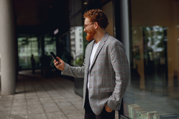 在休息时间，微笑的商人站在办公室附近拿着电话。高质量照片图片下载