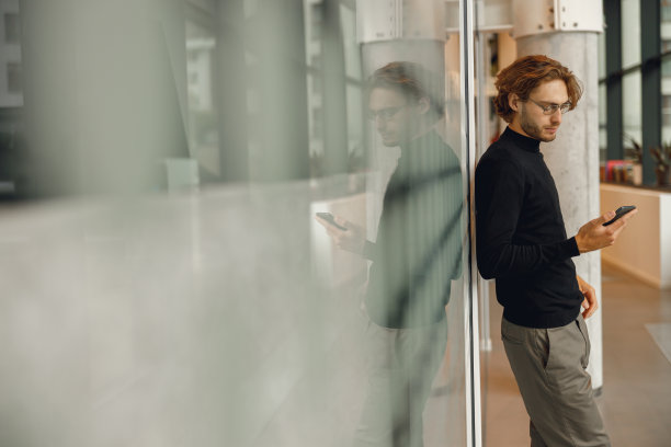 专注的商人在休息时间站在办公室拿着电话。高质量照片图片下载