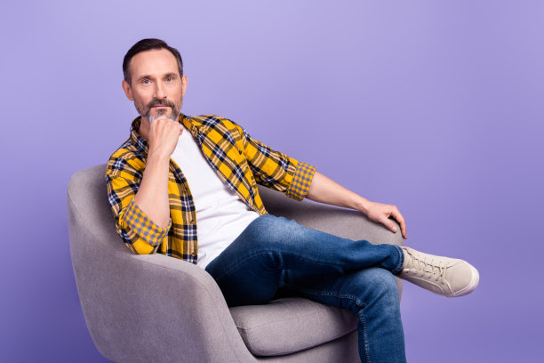 照片的时尚男子手摸下巴坐舒适扶手椅广告家具店空旷的空间孤立在紫色的背景图片下载