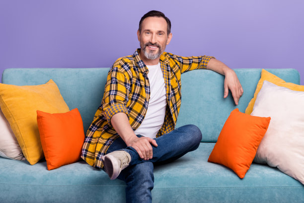 照片积极开朗的老人坐在舒适的沙发休息的新房子公寓房间孤立的紫色背景图片下载