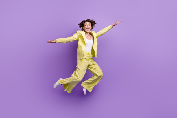 漂亮悠闲的女士穿西装外套跳高飞臂两侧孤立的紫罗兰色背景的全长照片图片下载