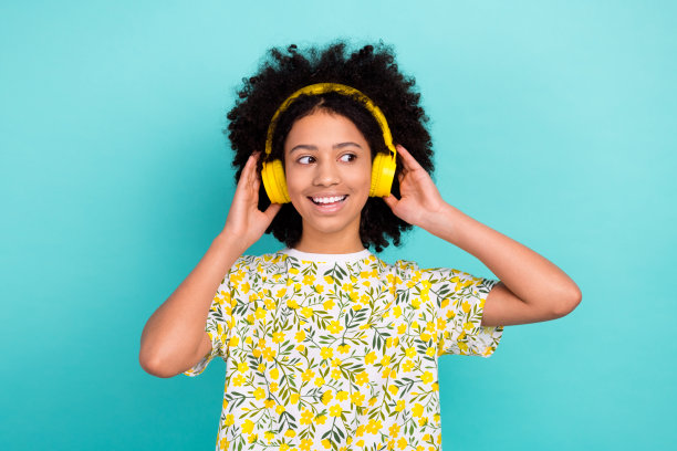 照片中无忧无虑的可爱女孩穿着时尚的印花衣服，听立体声播放列表，在青色的背景上看起来空无一物图片下载