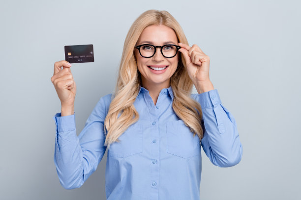 照片金发卷发女商人持有优质新银行卡nfc支付广告现代金融服务孤立在灰色背景图片下载