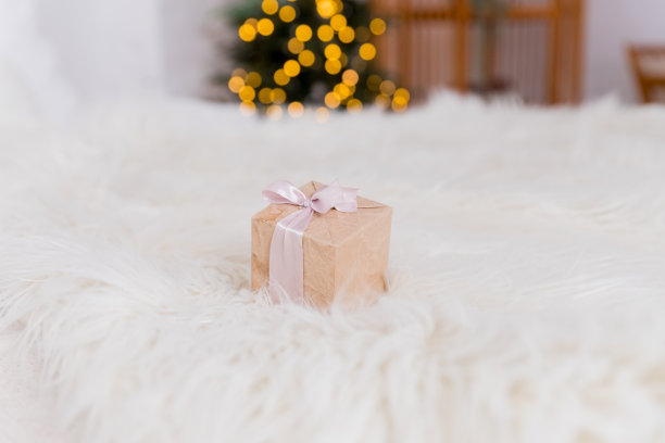 包裹好的圣诞礼物躺在舒适的床上，旁边是圣诞树，背景是美丽的模糊灯光。节日前夕的惊喜。在冬季给家人和朋友的礼物。图片下载