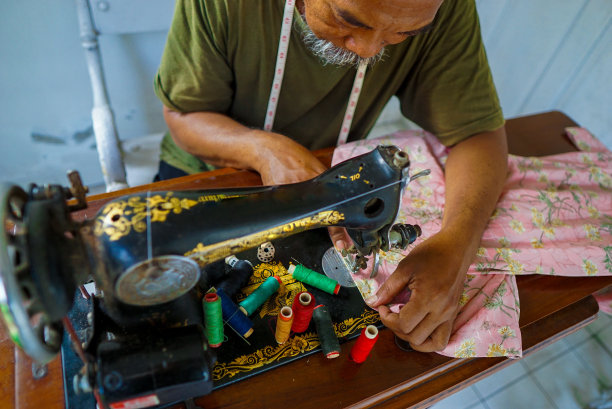 一位资深裁缝坐在缝纫机上缝纫。裁缝在缝纫机上工作。图片下载