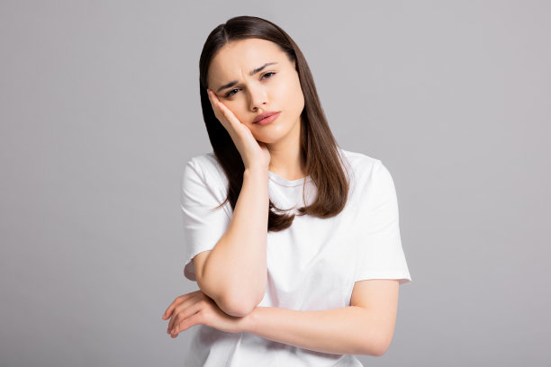 悲伤、疲惫、头痛、偏头痛的年轻女孩站在工作室的灰色背景上，孤立地闭上眼睛，手臂靠近头部图片下载