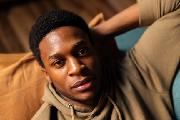 英俊的非裔美国人，深肤色的读者，一边在手机上享受好书，一边享受家中的舒适图片下载