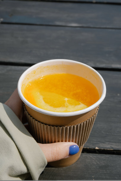 手持橙色水果茶杯与山的背景与复制空间为您的文字。高质量的垂直照片。图片下载