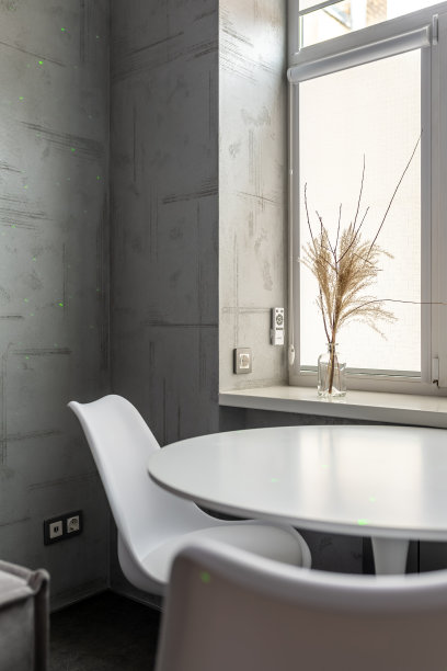 白色的圆桌靠窗而立，窗台上的一个花瓶里放着干枯的植物图片下载