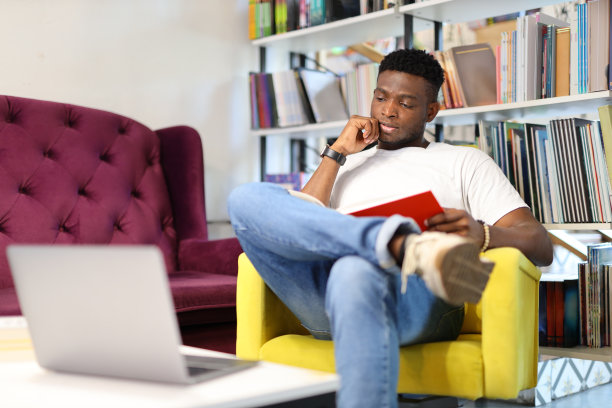 一个年轻人坐在家里的沙发上，用笔记本电脑上网学习和放松。图片下载