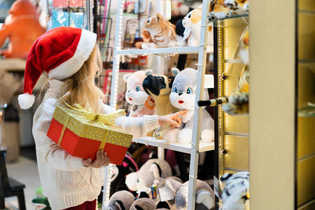 一个戴着圣诞帽、手里拿着新年礼物的小女孩站在玩具陈列柜前。孩子们为圣诞节挑选礼物。黑色星期五折扣图片下载