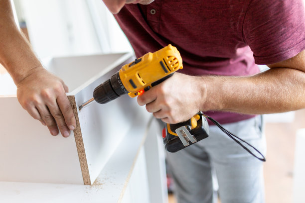 木匠用电动螺丝刀安装厨房的抽屉柜。家居装修概念。图片下载