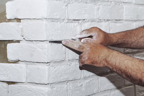 厨房墙上带倒角的白色瓷砖。瓷砖手在浴室墙上铺设白色矩形瓷砖的过程中。公寓和浴室的维修。图片下载