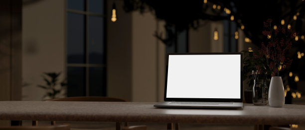 在夜晚的现代黑屋子里，桌子上放着一台白屏笔记本电脑。黑暗的工作空间，特写图像图片下载