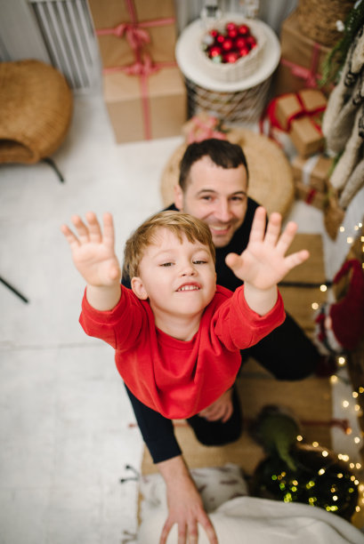 父亲在喜庆的房间里呕吐了蹒跚学步的小男孩。快乐的父亲带着小儿子庆祝新年的照片。圣诞树和装饰花环。装饰房子的内部。俯视图图片下载