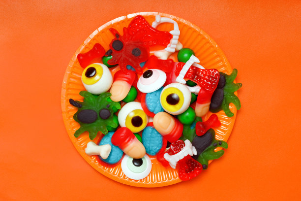 怪异的万圣节糖果:果冻手指糖，眼球，蜘蛛和脑糖在橙色背景。俯视图图片下载