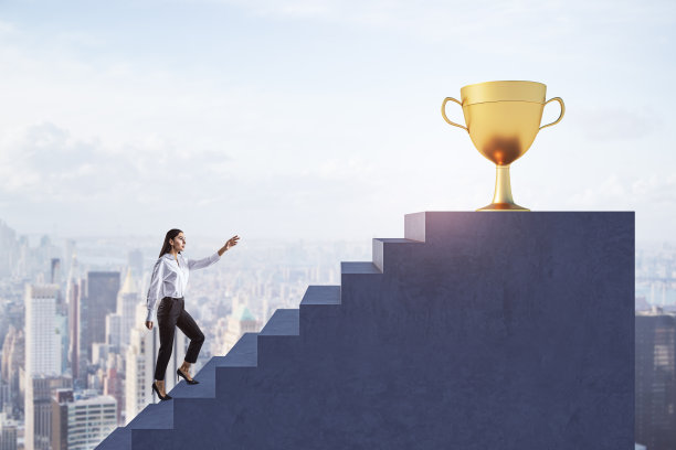 在模糊的城市背景下，年轻的欧洲女商人爬楼梯走向金色的冠军奖杯。成功与职业成长理念。图片下载