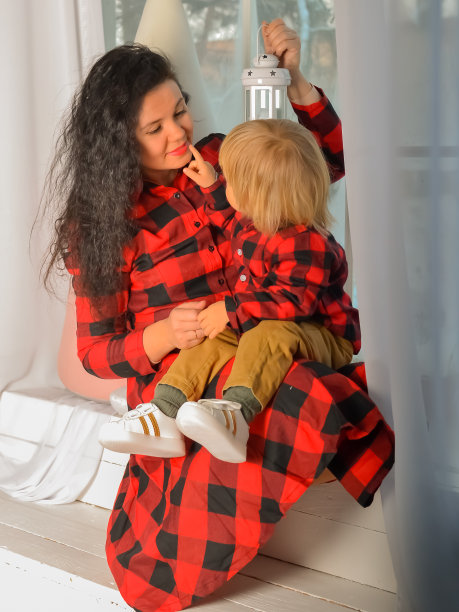 妈妈和儿子穿着相同的节日圣诞服装，坐在窗台上，拿着圣诞灯。家人看。圣诞奇迹。平安夜，母亲带着小儿子在家里望着窗外的照片。妈妈和孩子图片下载