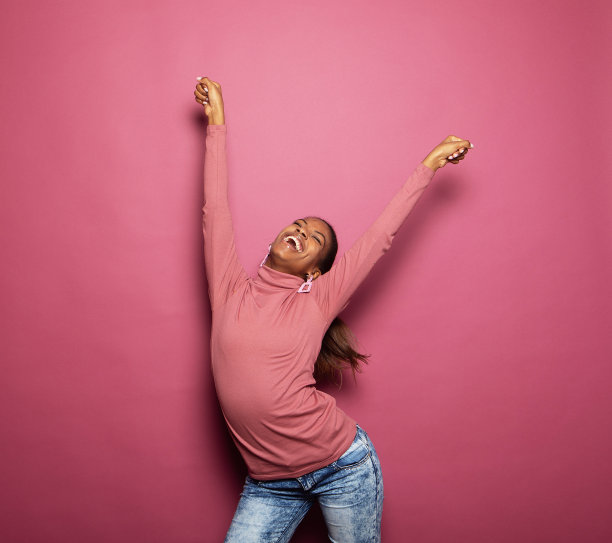 照片中年轻的非洲女子穿着休闲服跳舞，看起来空旷孤立的粉红色背景图片下载