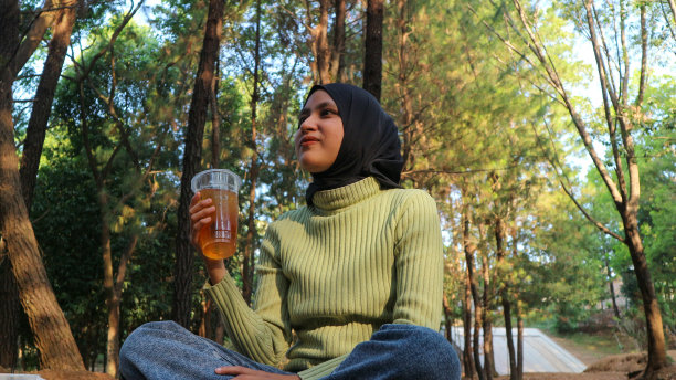 戴着头巾的穆斯林妇女手持茶杯坐在松树林中。图片下载