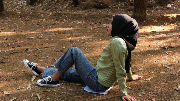 年轻的穆斯林妇女坐在草地上无忧无虑地休息，在阳光明媚的日子里在草坪上放松。侧视图图片下载