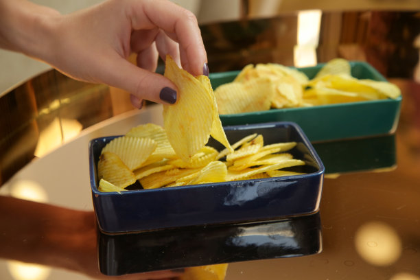 年轻悲伤的女人吃着不健康的零食，在客厅里吃着薯片。垃圾食品和不健康的饮食观念。图片下载